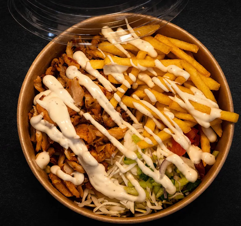 Kebabas lėkštėje iš viršaus: vištiena, bulvytės, daržovės ir baltas padažas dėžutėje